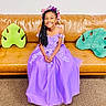 Queani is registered to the contest to win money with this photo: child, girl, smiling, dress, purple_dress, flower_crown, braided_hair, couch, leather_couch, green_pillow, leaf_pillow, indoor, carpet, happy, seated, portrait, home_decor, fashion, youth, cute