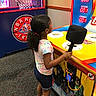 Quiari joined the competition — help win amazing prizes! arcade, basketball_hoop, black_hair, carpet, child, curly_hair, entertainment, game, girl, indoor, playing, scoreboard, shoes, shorts, side_view, socks, superhero_graphics, tie_dye_shirt, toy_hammer, yellow_game_machine