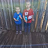 children, boys, siblings, portrait, outdoor, wooden_deck, fence, smiling, standing, blue_shirt, red_shirt, sportswear, nike_shirt, cup, drink, shoes, short_hair, backyard, daylight, casual