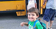 Braylyn is registered to the contest to win money with this photo: adult, asphalt, backpack, boarding, casual_clothing, child, children, family, morning, outdoor, portrait, school, school_bus, school_day, schoolboy, smiling, street, transportation, travel, yellow_bus