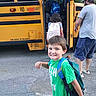 Braylyn is registered to the contest to win money with this photo: child, schoolboy, smiling, backpack, school_bus, school, boarding, outdoor, transportation, yellow_bus, adult, children, family, morning, street, asphalt, school_day, casual_clothing, portrait, travel