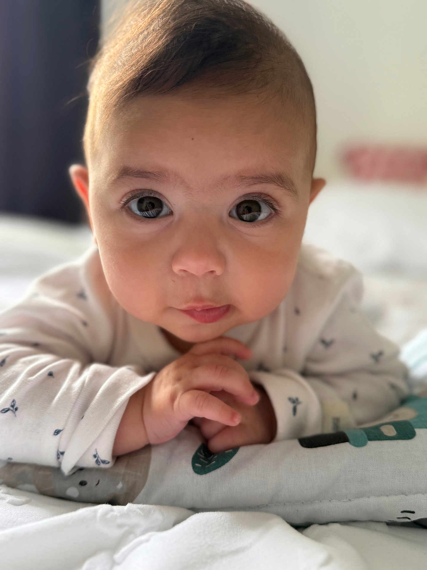 Dahlia Mila is registered to the contest to win money with this photo: baby, infant, face, hands, eyes, cute, lying_down, white_clothing, soft_light, bed, blanket, patterned_blanket, indoors, portrait, closeup, skin, curious, child, young, person