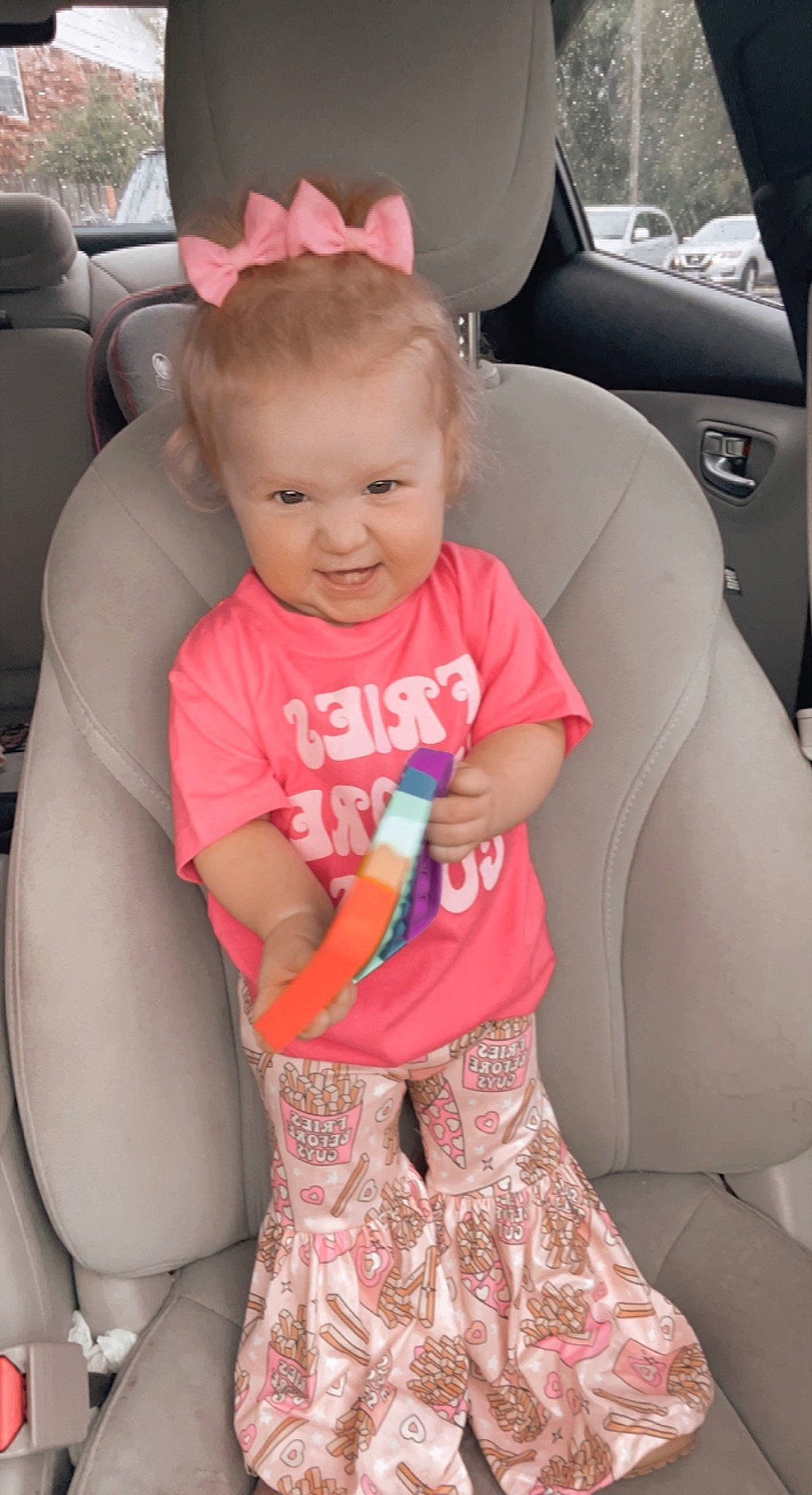 Oaklynn is registered to the contest to win money with this photo: arm, black, car, car_seat_cover, comfort, finger, hair, head, joint, leg, mammal, person, pink, product, shoe, skin, smile, thigh, toddler, vehicle_door