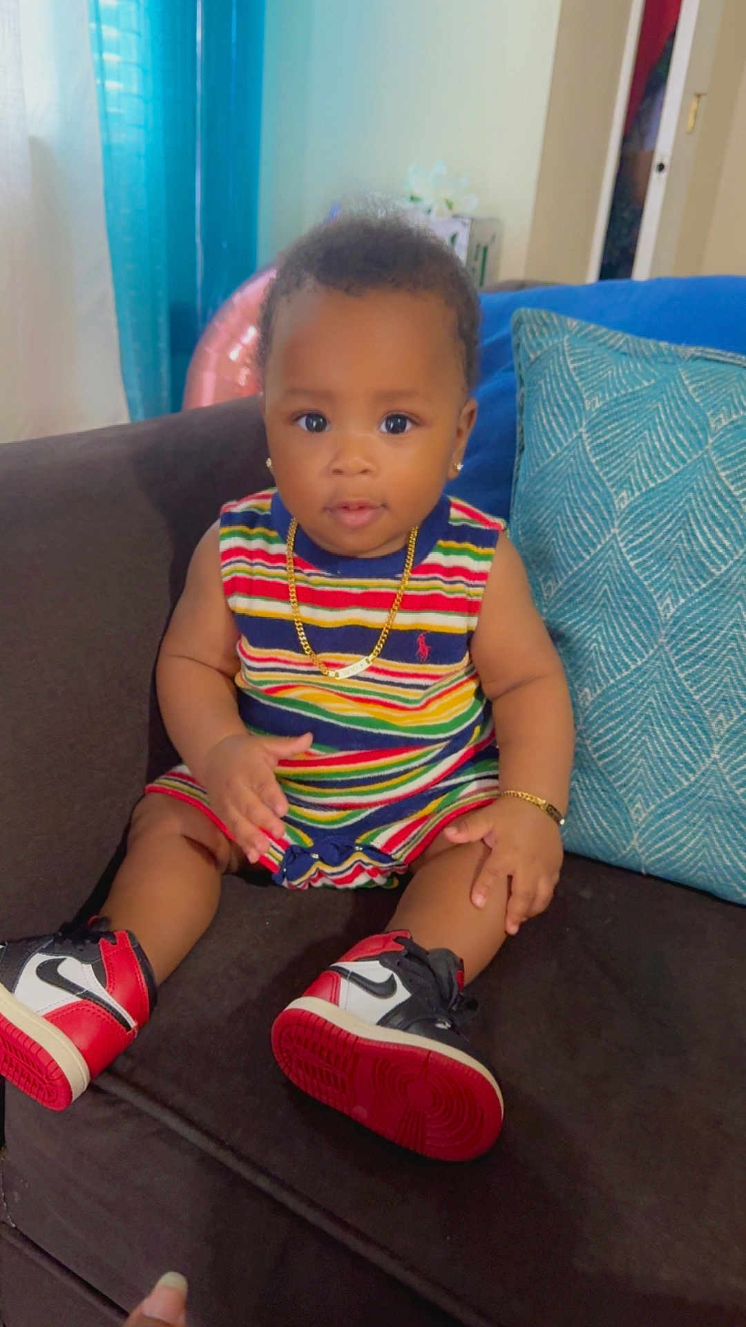 Damir is registered to the contest to win money with this photo: baby, child, sitting, couch, striped_clothing, sneakers, gold_jewelry, bracelet, necklace, earrings, pillow, indoor, curtains, colorful, portrait, infant, cute, smiling, furniture, person
