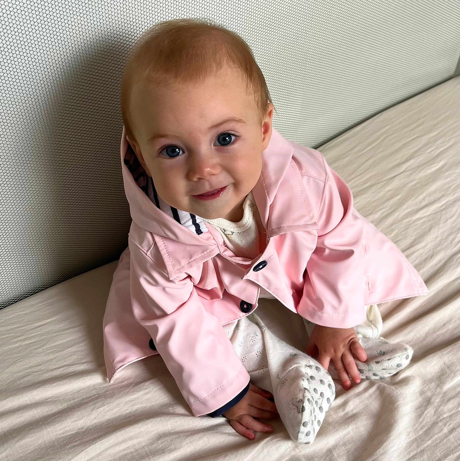 Adèle a rejoint le concours — aidez-le/la à gagner de superbes lots ! baby, child, infant, pink_jacket, bed, smile, blue_eyes, cute, clothing, sitting, indoors, portrait, hands, feet, white_outfit, soft_lighting, happy, young, person, closeup