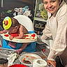 Apollo joined the competition — help win amazing prizes! baby, high_chair, party_hat, food, messy, woman, smiling, indoor, table, plate, paper_towel, food_spill, meal, child, person, celebration, dining, kitchen, happy, casual