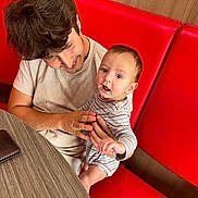 Apollo joined the competition — help win amazing prizes! baby, child, young_man, striped_clothing, red_booth, wooden_wall, table, smile, curious, indoor, holding, person, seated, casual_clothing, portrait, tender_moment, family, human, happy, face