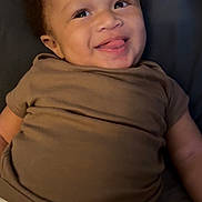 Jalen is registered to the contest to win money with this photo: baby, smiling, tongue_out, brown_shirt, diaper, child, happy, lying_down, infant, cute, portrait, skin, face, person, indoors, young_child, cheerful, expression, clothing, baby_girl
