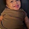 baby, smiling, tongue_out, brown_shirt, diaper, child, happy, lying_down, infant, cute, portrait, skin, face, person, indoors, young_child, cheerful, expression, clothing, baby_girl