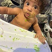 Jayton is registered to the contest to win money with this photo: toddler, child, high_chair, messy, food, green_food, face, hand, curly_hair, wide_eyes, indoor, expression, baby, table, feeding, skin, person, cute, looking, surprised