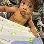 toddler, child, high_chair, messy, food, green_food, face, hand, curly_hair, wide_eyes, indoor, expression, baby, table, feeding, skin, person, cute, looking, surprised