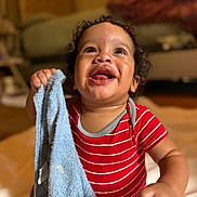 Jayton is registered to the contest to win money with this photo: baby, blanket, child, cozy, curly_hair, cute, expression, face, happy, home, indoor, infant, person, red_clothing, sitting, smiling, soft_lighting, striped, towel, young_child
