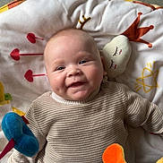 Ishaïm a rejoint le concours — aidez-le/la à gagner de superbes lots ! baby, child, smiling, plush_toy, blanket, striped_sweater, indoor, cute, happy, face, head, person, infant, cozy, soft_toy, green_pants, floor, dim_light, playtime, cheeks