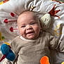 baby, child, smiling, plush_toy, blanket, striped_sweater, indoor, cute, happy, face, head, person, infant, cozy, soft_toy, green_pants, floor, dim_light, playtime, cheeks