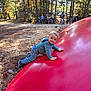 Myles is registered to the contest to win money with this photo: toddler, child, smiling, hoodie, jeans, shoes, inflatable, red, climbing, outdoor, forest, trees, autumn, leaves, people, golf_cart, sunlight, nature, playground, recreation