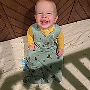 Myles is registered to the contest to win money with this photo: baby, infant, smiling, sleeping_sack, yellow_shirt, crib, wooden_crib, pacifier, patterned_sheet, bear_pattern, happy, child, indoors, shadow, lighting, cute, toddler, face, sitting, bedtime