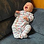 baby, onesie, smiling, laughing, couch, blue, furniture, infant, happy, child, indoors, cozy, text_pattern, apparel, person, seat, cute, relaxed, comfort, joy