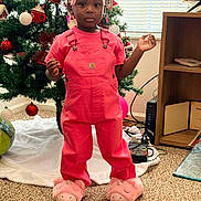 Autumn joined the competition — help win amazing prizes! child, girl, toddler, pink_overalls, unicorn_slippers, christmas_tree, ornaments, braided_hair, hair_beads, window_blinds, bookshelf, carpet, living_room, holiday_decor, standing, portrait, indoors, neutral_expression, game_controller, pink_color