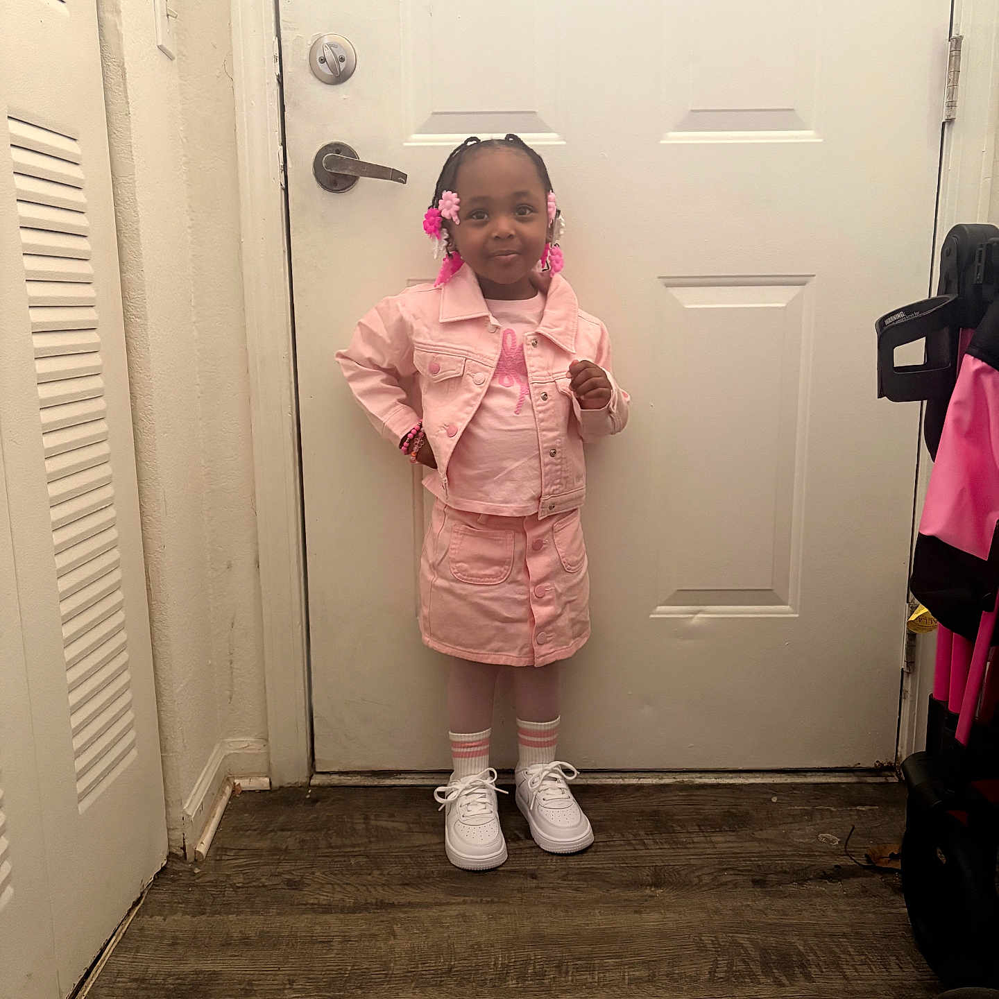 Autumn is registered to the contest to win money with this photo: child, girl, pink_clothing, denim_jacket, skirt, white_sneakers, striped_socks, standing, posing, hair_beads, flower_beads, indoors, door, floor, wall, bracelet, smiling, confident, home, fashion