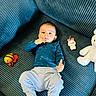 baby, child, infant, portrait, sitting, lying_down, sofa, couch, blue, clothing, shirt, pants, thumbs_up, smiling, toys, teddy_bear, bee_toy, indoor, living_room, safe