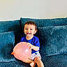 child, toddler, baby, smiling, face_paint, balloon, sofa, couch, sitting, indoors, portrait, happy, blue_clothing, white_shorts, barefoot, brown_hair, face, furniture, playful, photography