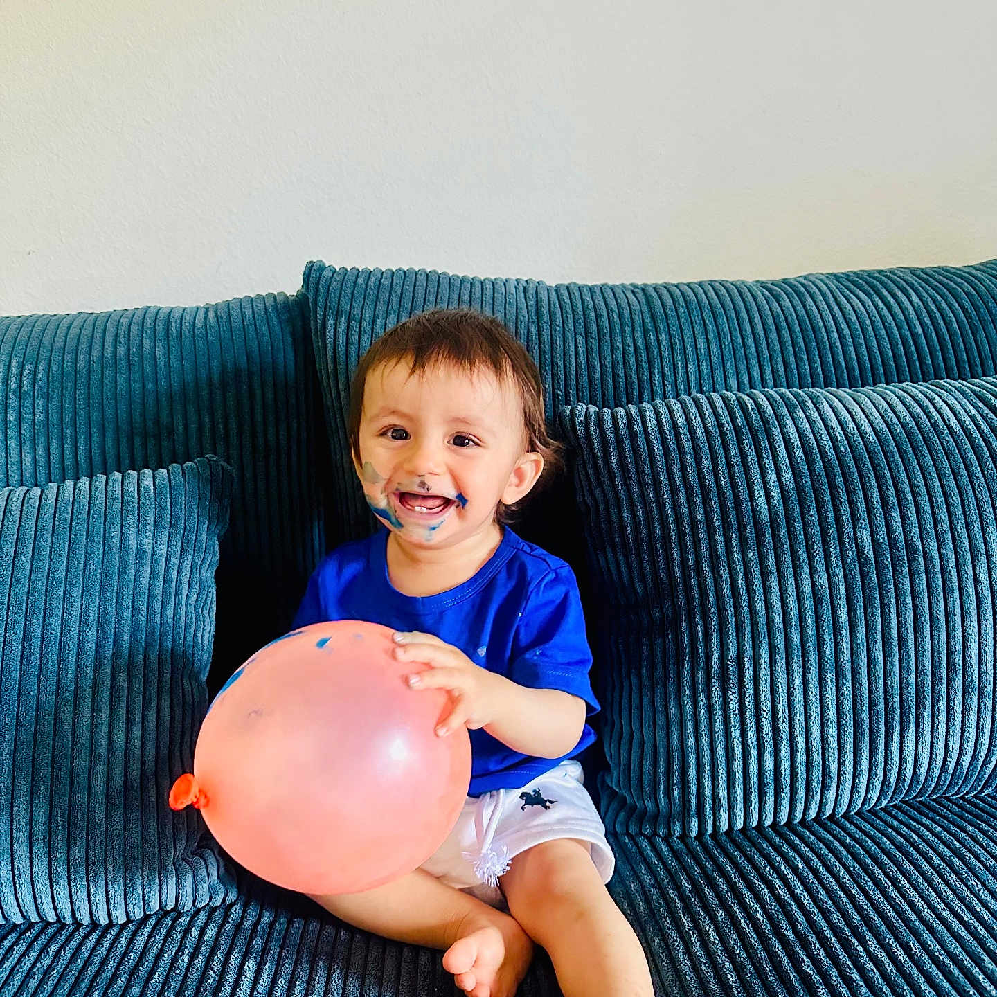 Maher joined the competition — help win amazing prizes! child, toddler, baby, smiling, face_paint, balloon, sofa, couch, sitting, indoors, portrait, happy, blue_clothing, white_shorts, barefoot, brown_hair, face, furniture, playful, photography
