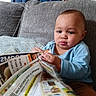 Benjamin is registered to the contest to win money with this photo: baby, child, infant, sitting, couch, sofa, cushion, blue_shirt, indoors, home, curtains, grocery_flyers, newspaper, paper, shopping, reading, hands, portrait, serious_expression, cozy