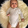 baby, infant, onesie, sheep_pattern, fluffy_rug, white_rug, smiling, happy, lying_down, cute, child, person, skin, head, arms, legs, indoors, soft_texture, comfortable, peaceful