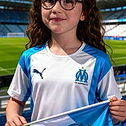 Louna a rejoint le concours — aidez-le/la à gagner de superbes lots ! child, girl, glasses, curly_hair, stadium, flag, sports, soccer, team_jersey, blue_and_white, outdoor, smile, fan, young, happy, daytime, spectator, holding_flag, athletic, event