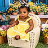 Alora is registered to the contest to win money with this photo: baby, child, yellow_dress, armchair, flowers, basket, green_grass, curly_hair, headband, earrings, window, blue_shutters, spring, portrait, indoor, smiling, sitting, cute, colorful, decor
