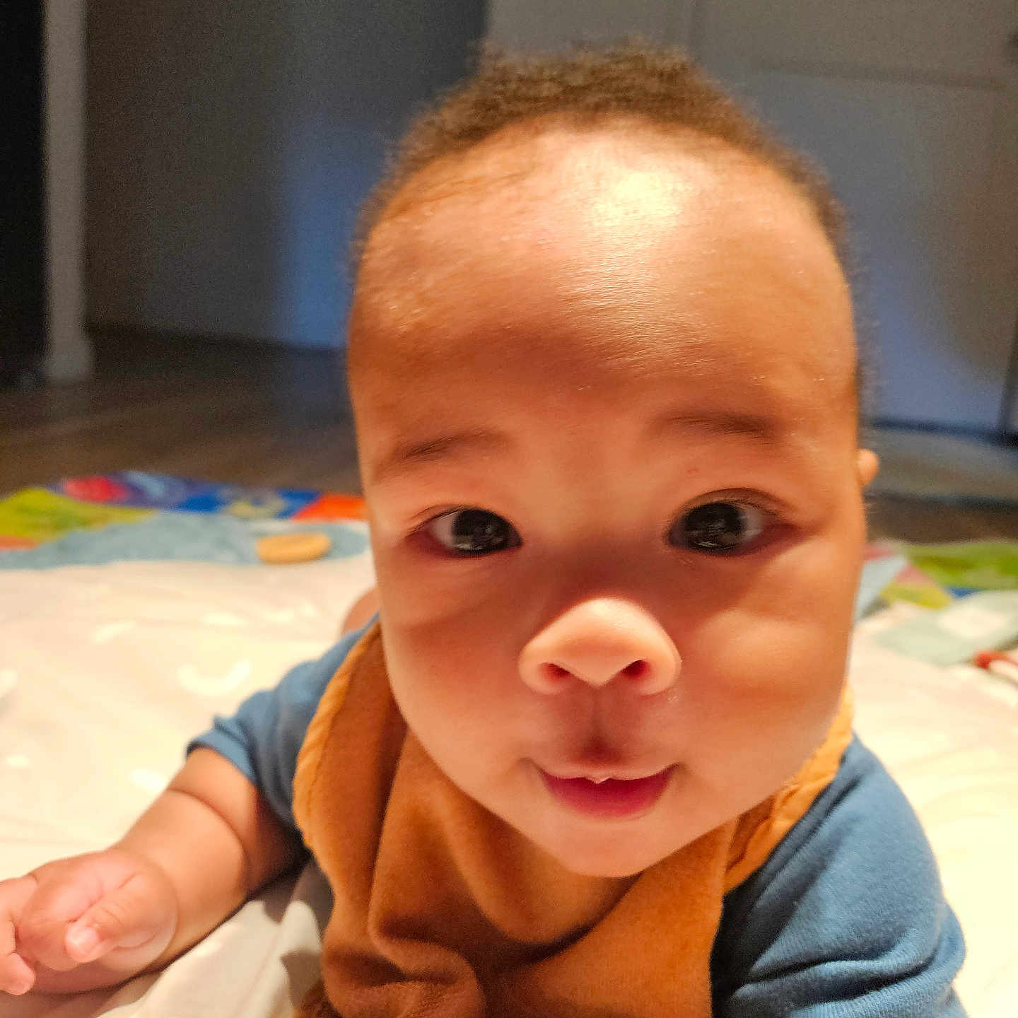 James joined the competition — help win amazing prizes! baby, bib, blanket, child, closeup, clothing, curious, cute, expression, eyes, face, floor, hand, head, indoor, infant, mouth, person, skin, toddler