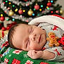 Aria is registered to the contest to win money with this photo: baby, sleeping, christmas_tree, holiday, presents, blanket, santa_hat, toy, gingerbread_man, reindeer_toy, festive, cozy, infant, smiling, cute, indoors, celebration, decorations, christmas_lights, soft