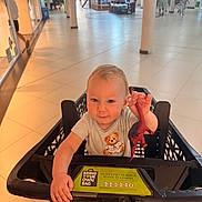Oscar-Dayne is registered to the contest to win money with this photo: toddler, child, shopping_cart, toy, dinosaur, mall, shopping, floor, tiled_floor, person, baby, clothing, indoor, footwear_free, holding, cute, smiling, retail, aisle, store