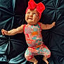 Oaklynn is registered to the contest to win money with this photo: baby, infant, child, headband, red_bow, colorful_outfit, smile, face, arm, leg, barefoot, tufted_surface, dark_background, lying_down, happy, cute, skin, expression, one_person, indoors
