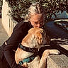 Bob participe au concours pour gagner de l'argent avec cette photo : dog, person, woman, glasses, hugging, cuddling, outdoor, garden, sunlight, wall, leash, harness, collar, golden_dog, light_brown_fur, sitting, affection, portrait, trees, backyard