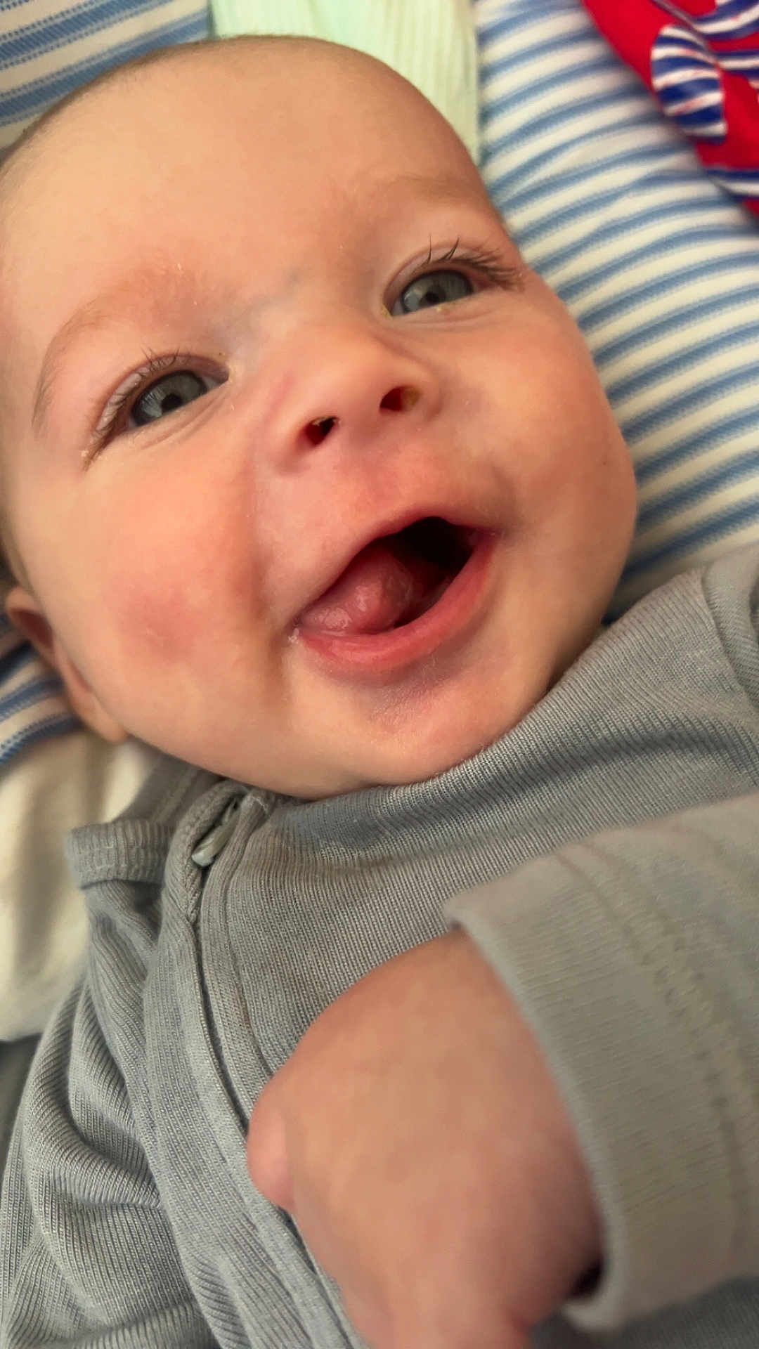 Zaiden joined the competition — help win amazing prizes! baby, close_up, smile, happy, infant, face, eyes, skin, clothing, gray_outfit, hand, lying_down, striped_background, blue, white, cute, joyful, portrait, young_child, human