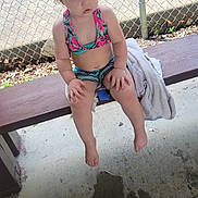 Dakota Gillam joined the competition — help win amazing prizes! toddler, child, swimsuit, bench, outdoor, fence, towel, water, concrete, curly_hair, summer, sitting, barefoot, expression, daylight, shade, play_area, young_child, casual, relaxed