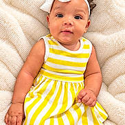 Empress is registered to the contest to win money with this photo: baby, infant, child, portrait, smiling, sitting, headband, bow, striped_dress, yellow_clothing, white_clothing, blanket, indoors, close_up, face, eyes, hair, hand, photography, adorable
