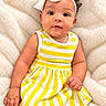 baby, infant, child, portrait, smiling, sitting, headband, bow, striped_dress, yellow_clothing, white_clothing, blanket, indoors, close_up, face, eyes, hair, hand, photography, adorable