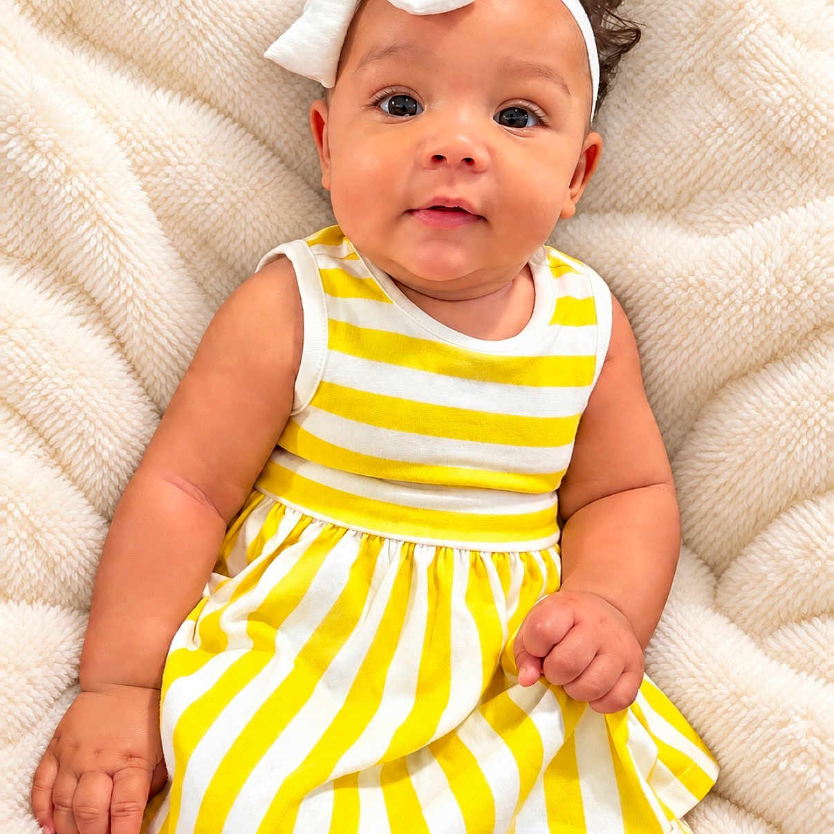 Empress is registered to the contest to win money with this photo: baby, infant, child, portrait, smiling, sitting, headband, bow, striped_dress, yellow_clothing, white_clothing, blanket, indoors, close_up, face, eyes, hair, hand, photography, adorable