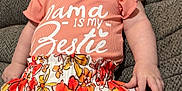 Lauren is registered to the contest to win money with this photo: baby, child, smiling, sitting, couch, clothing, floral_skirt, peach_shirt, text_on_clothing, indoor, infant, cute, happy, person, portrait, furniture, skin, hand, face, head