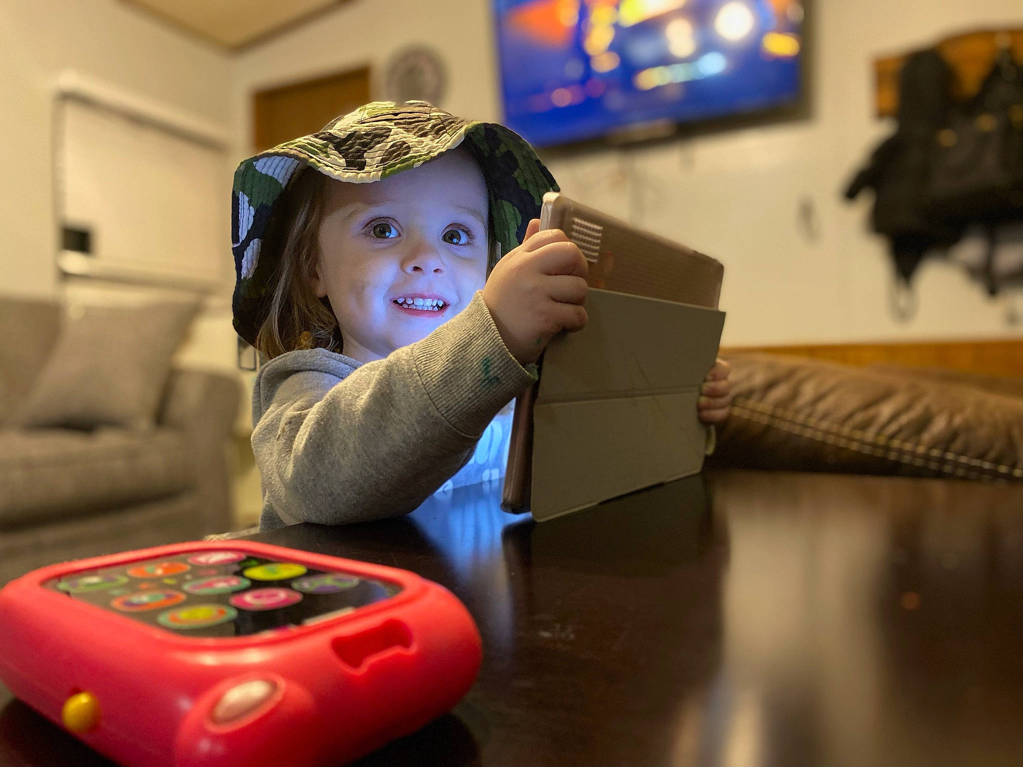 Londyn is registered to the contest to win money with this photo: audio_equipment, baby_playing_with_toys, black, cap, child, comfort, couch, electronic_device, floor, flooring, fun, gadget, happy, headwear, joy, person, picture_frame, sitting, smile, television