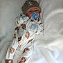 baby, infant, pacifier, onesie, hat, football_pattern, blanket, sleepwear, cute, lying_down, gloves, footwear, indoors, soft_texture, newborn, child, portrait, cozy, comfort, sleeping_area