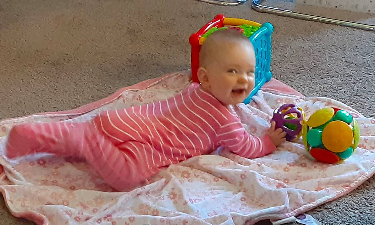 Estella-mae is registered to the contest to win money with this photo: baby, baby_playing_with_toys, baby_products, baby_toddler_clothing, baby_toys, ball, child, comfort, dress, fun, grass, happy, linens, pattern, person, play, room, sitting, smile, toddler