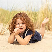 Léonie participe au concours pour gagner de l'argent avec cette photo : child, curly_hair, sand, beach_grass, outdoor, smile, happy, portrait, young_child, nature, summer, casual_clothing, barefoot, relaxed, daylight, person, head, face, skin, playful