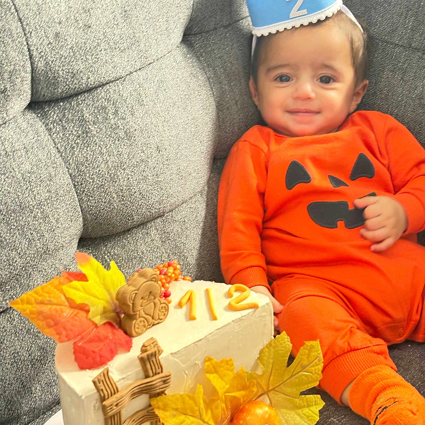Yamen Almukhtar is registered to the contest to win money with this photo: autumn_leaves, baby, blue_crown, cake, celebration, cute, fall_theme, festive, gray_couch, half_birthday, holiday, indoor, infant, orange_outfit, portrait, pumpkin_costume, pumpkin_decoration, sitting, smiling, teddy_bear_cookie