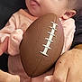 baby, infant, football, hands, pajamas, person, child, cute, holding, soft_lighting, indoor, closeup, skin, fingers, face, looking, expression, small_football, adult, comfort