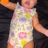 baby, infant, child, onesie, floral_pattern, toy, colorful, blue_eyes, lying_down, curious, cute, skin, arm, legs, indoors, portrait, young_child, playful, expression, background