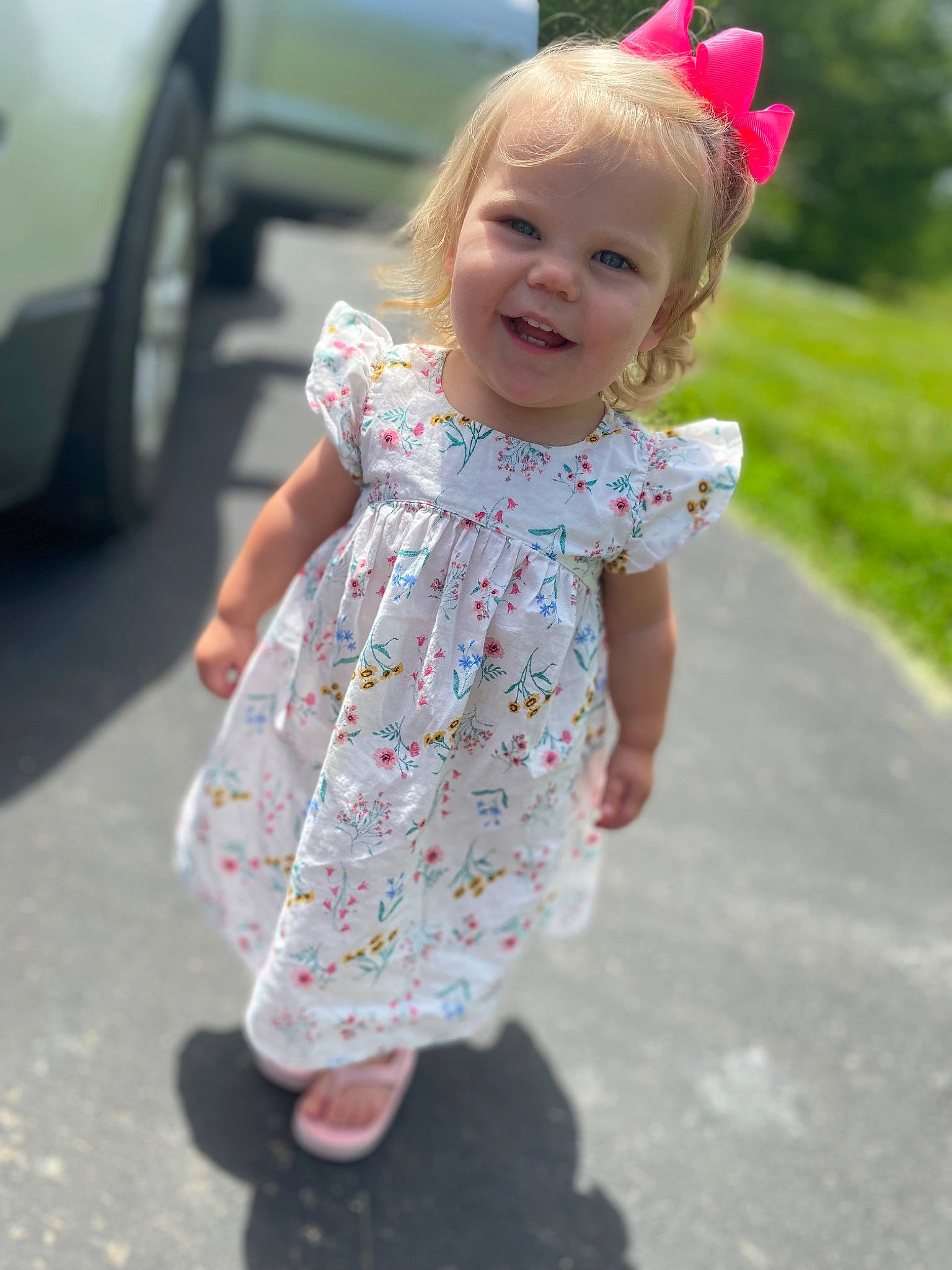Brinkley is registered to the contest to win money with this photo: automotive_tire, baby_toddler_clothing, dress, eye, face, facial_expression, hair, hairstyle, happy, head, joint, joy, person, photograph, pink, plant, skin, sleeve, smile, standing