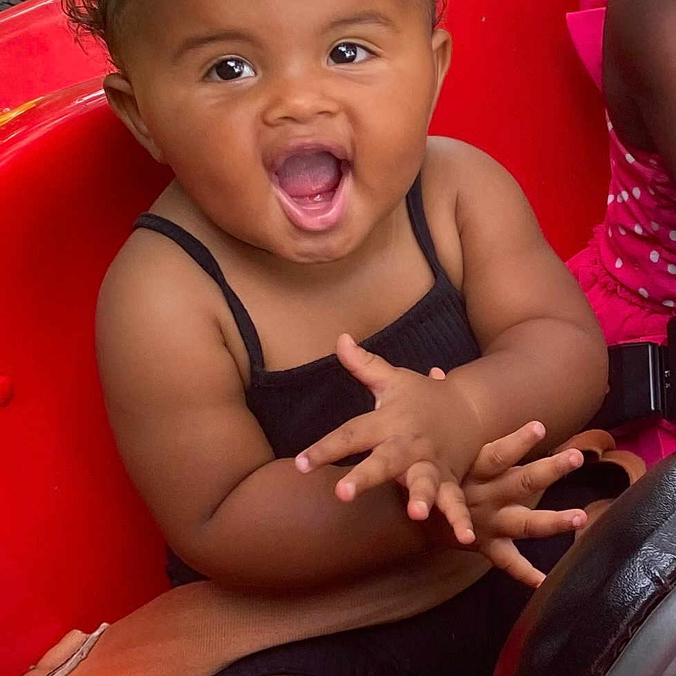 Ariel joined the competition — help win amazing prizes! black_outfit, child, clapping, curly_hair, cute, driving_wheel, friend, fun, grass, happy, joy, outdoor, person, play, red_toy_car, seatbelt, sitting, smiling, summer, toddler